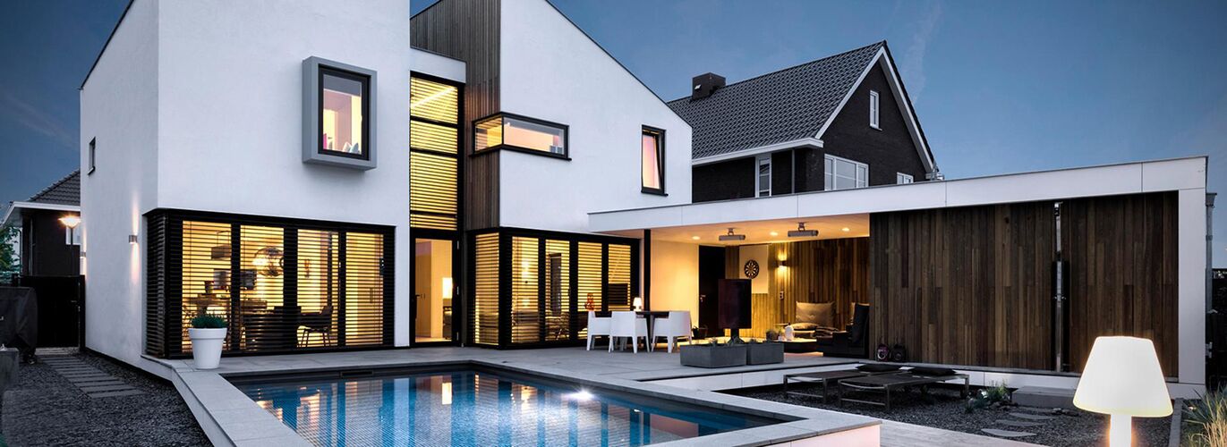 Modernes Wohnhaus mit Terrasse und Pool, hell erleuchteten Fenstern und herabgelassenen Raffstores