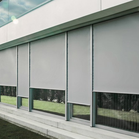 Außenansicht einer Fensterfront mit halb geschlossenen grauen Textilscreens