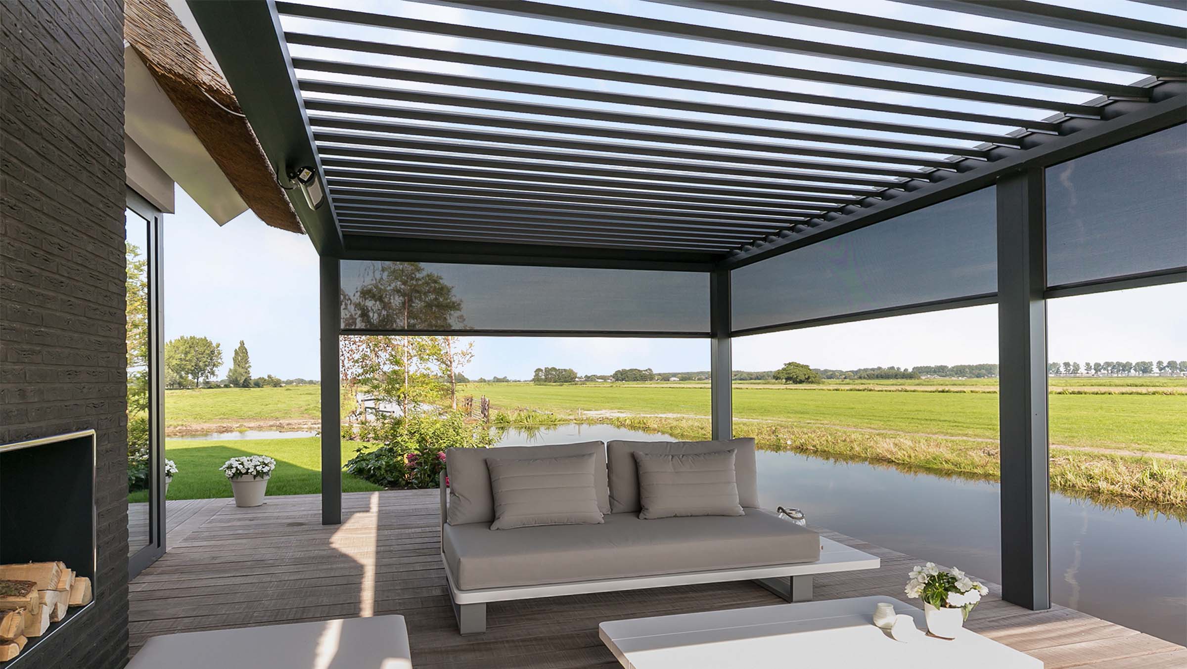Lamellendach-Pergola mit seitlichen Textilscreens als Überdachung einer Terrasse am Wasser
